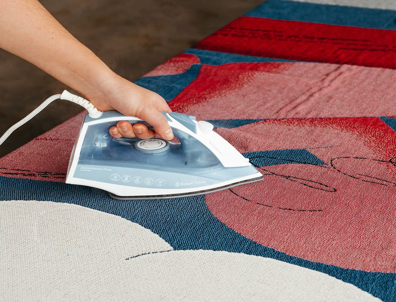 Person ironing a woven throw with an iron