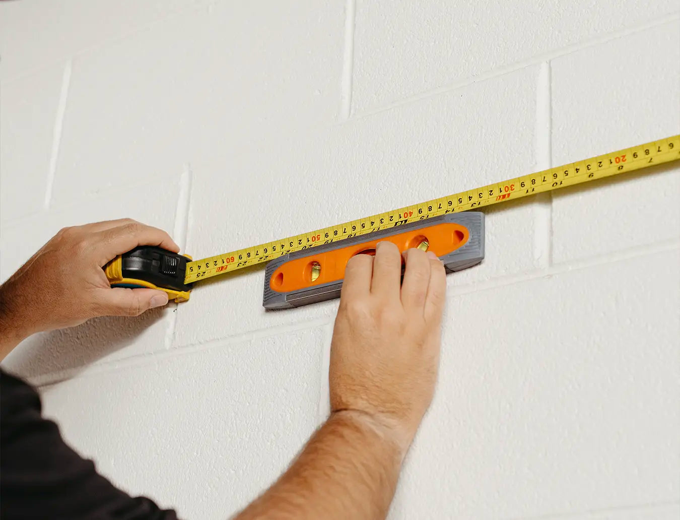 Person measuring wall markings with a measuring tape and spirit level.