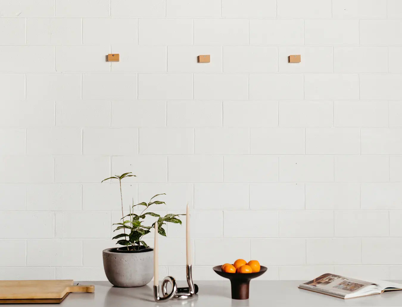 3 Slowdown Studio blanket hanger clips mounted onto a white brick wall.