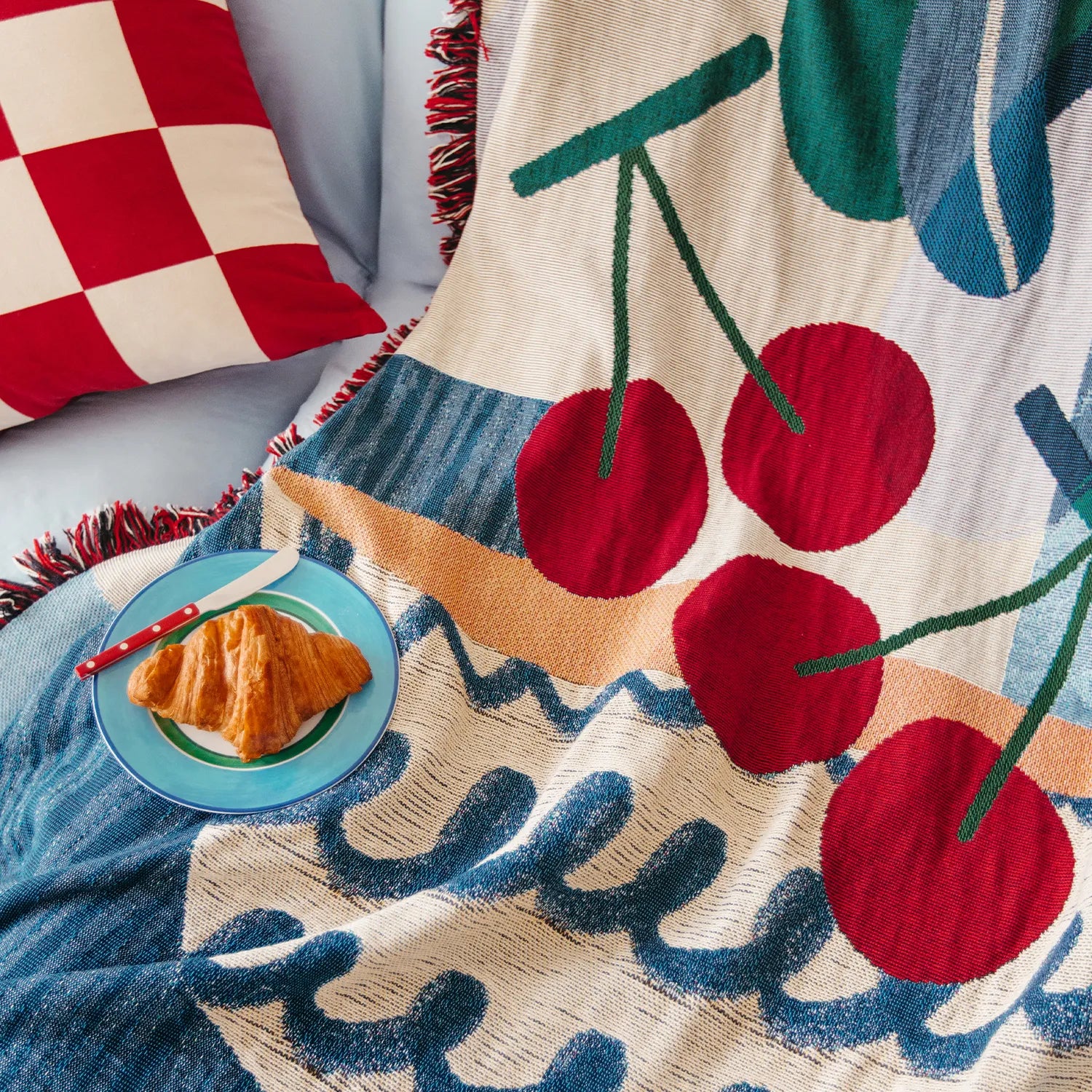 Colorful blanket with cherry design on a couch with a plate of food.