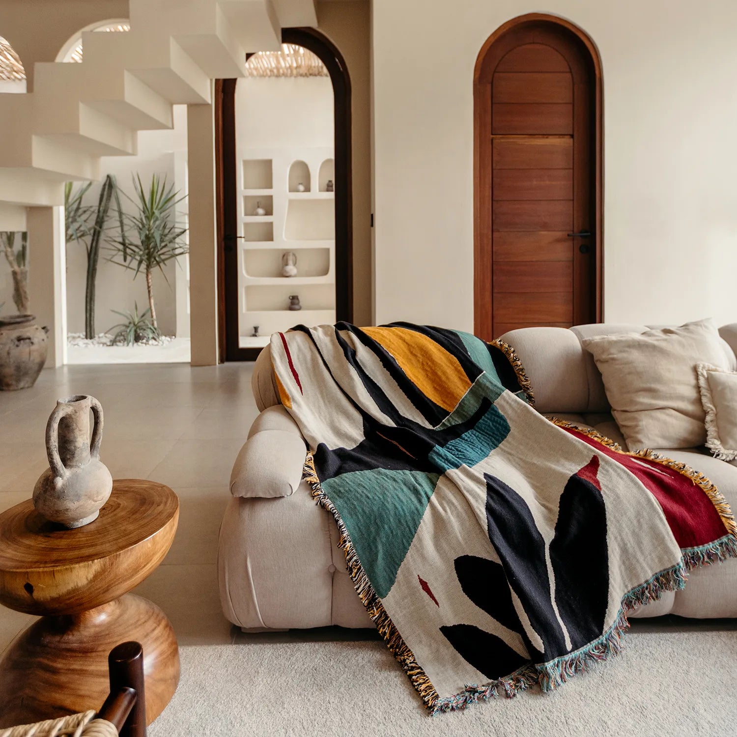 Living room with a beige sofa draped with a colorful blanket, wooden side table, and decorative elements.