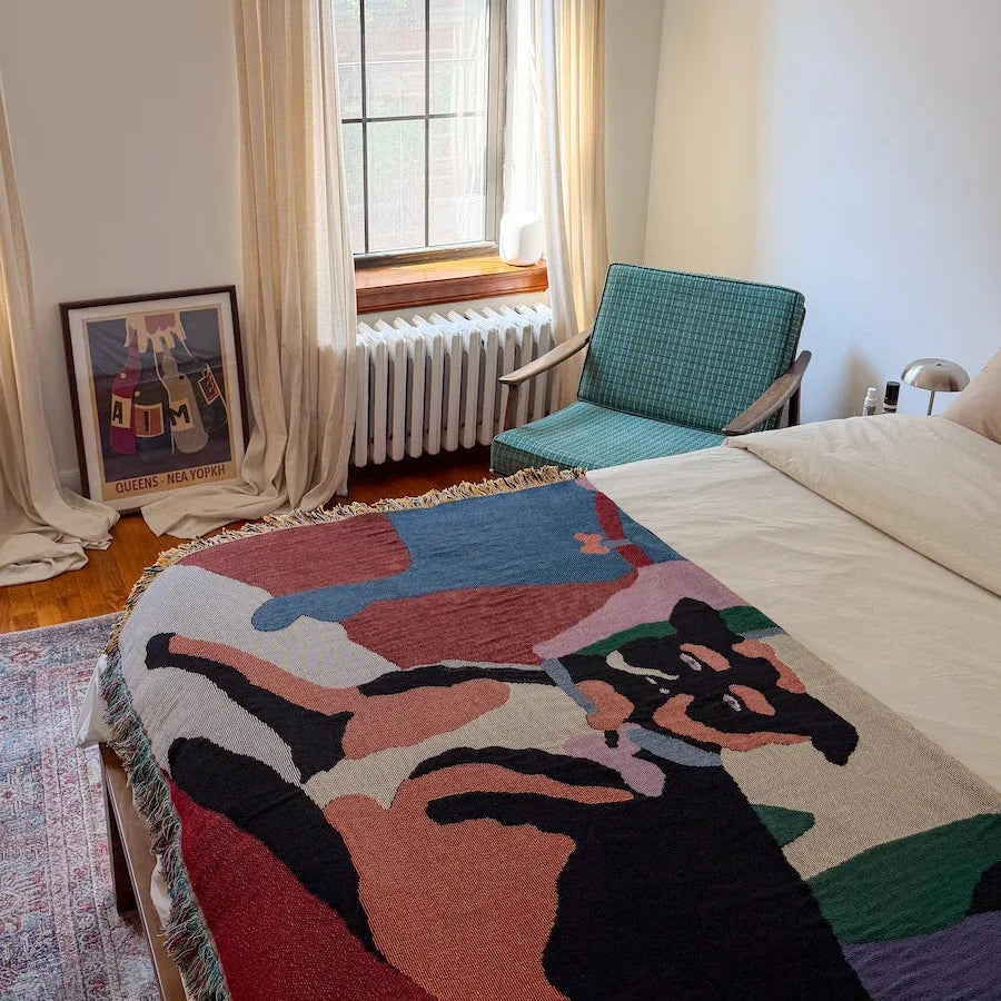 Bedroom with a colorful bed blanket, chair, and window with curtains.