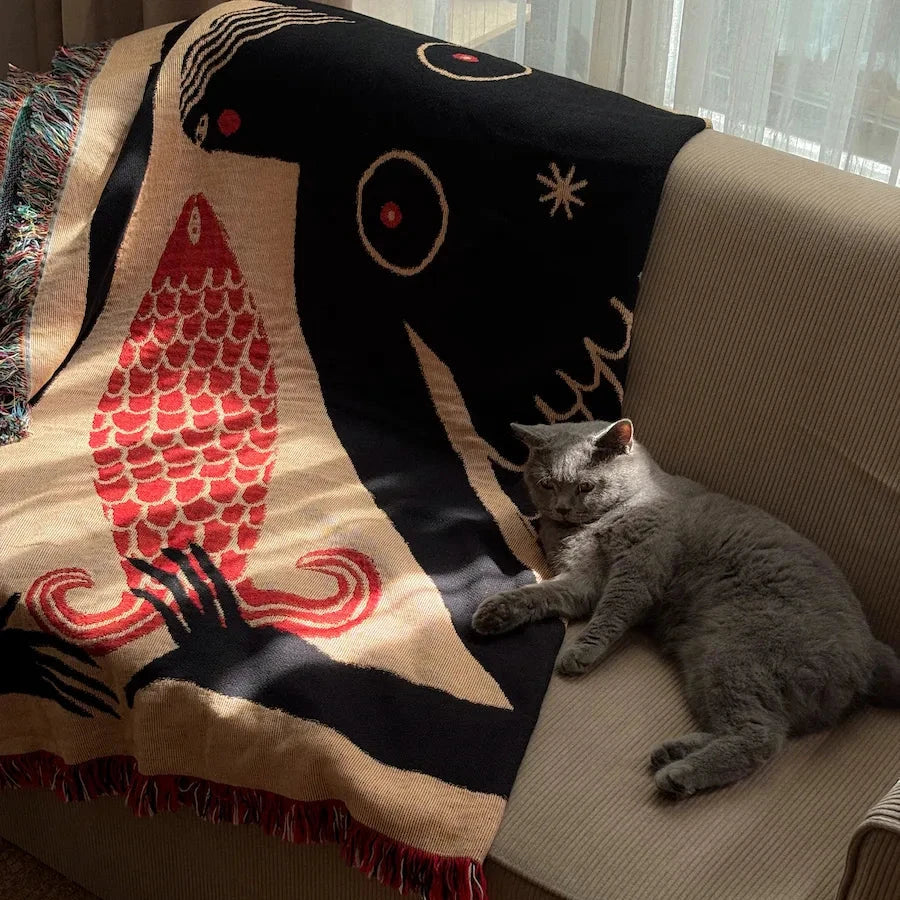Gray cat lying on a couch with a decorative blanket featuring abstract designs.