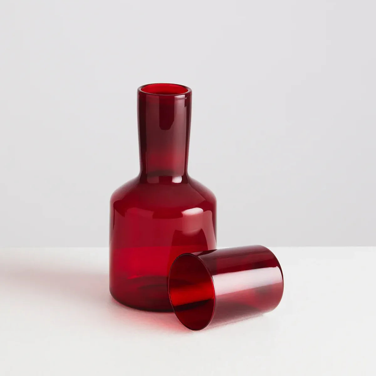 Red glass carafe and glass on a light gray background