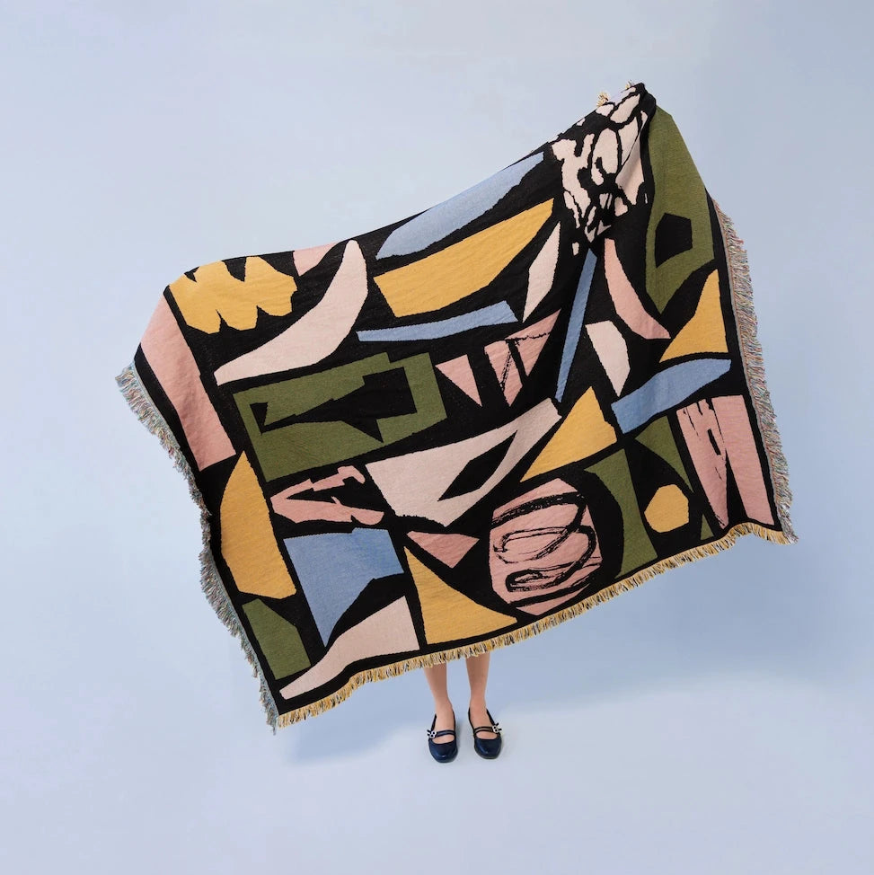 Colorful abstract-patterned blanket draped over a person on a light blue background