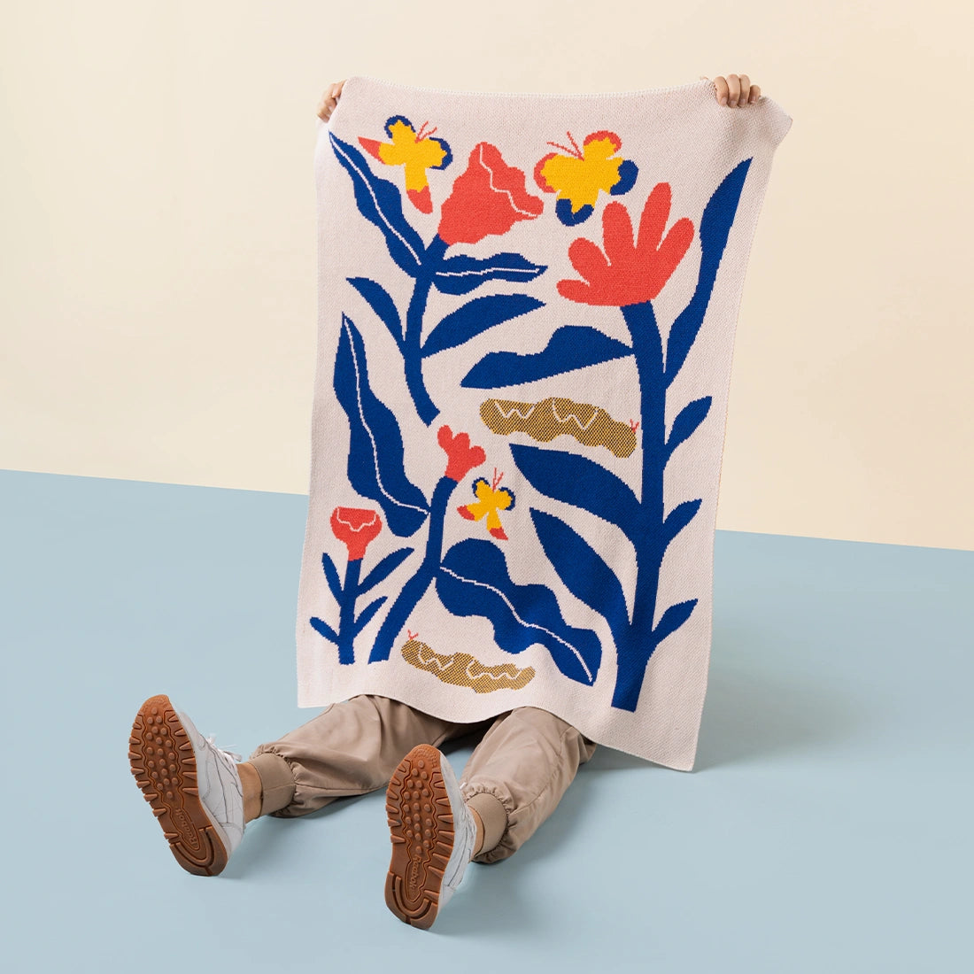 Person holding a colorful kids blanket with a flower and butterfly motif in red, blue and yellow against a light background