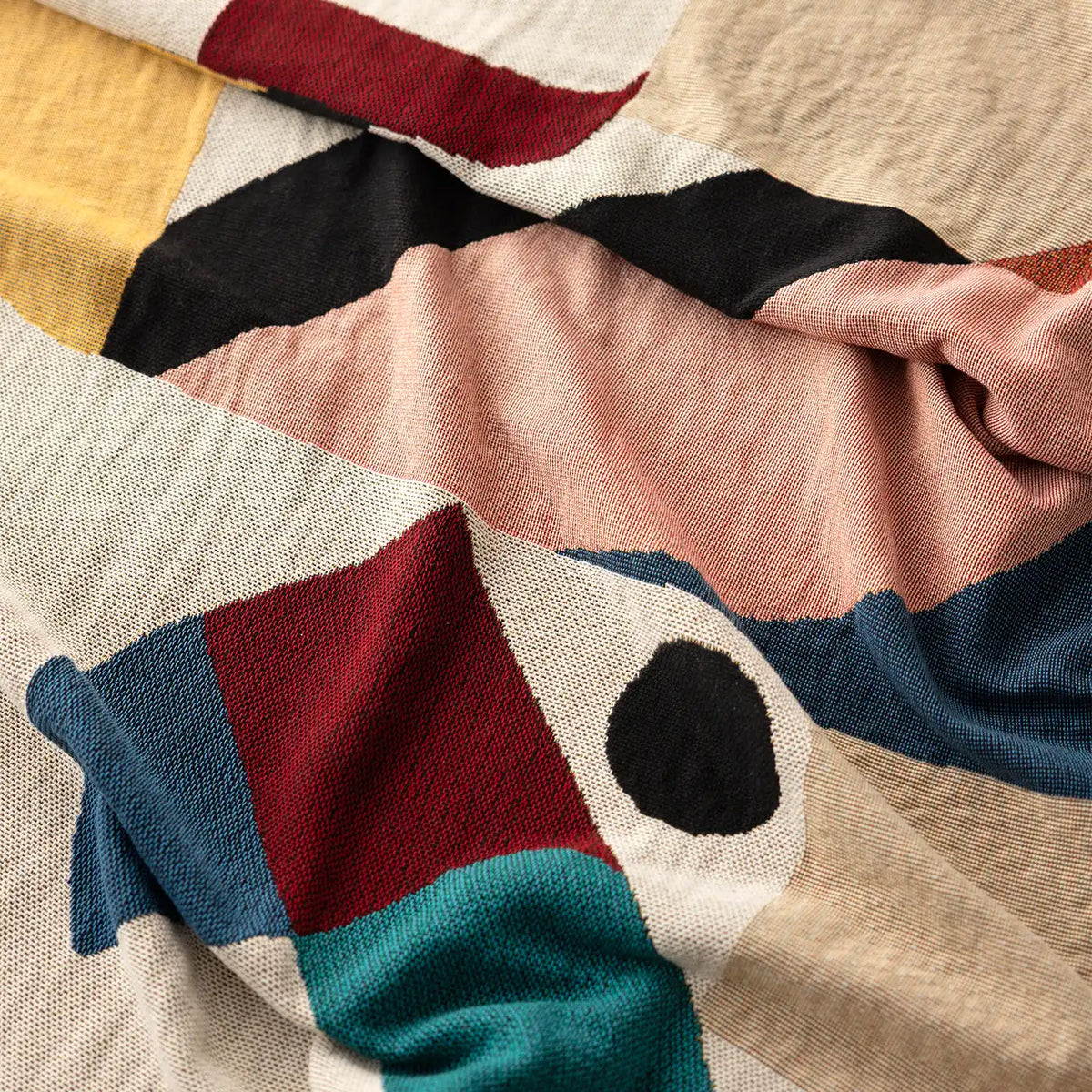 A close-up of the Slowdown Studio Pierre blanket or throw with an abstract geometric pattern in beige, blush pink, black, blue, teal, and red.