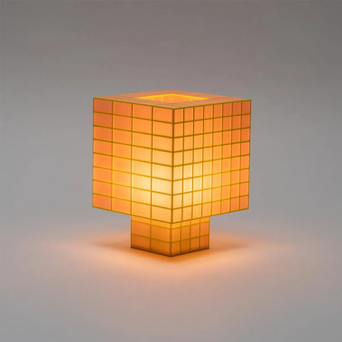A Ridezign Tesser 8:3 table lamp with a cube-shaped shade and matching base, made of glowing warm orange translucent square panels, set against a neutral gray background.