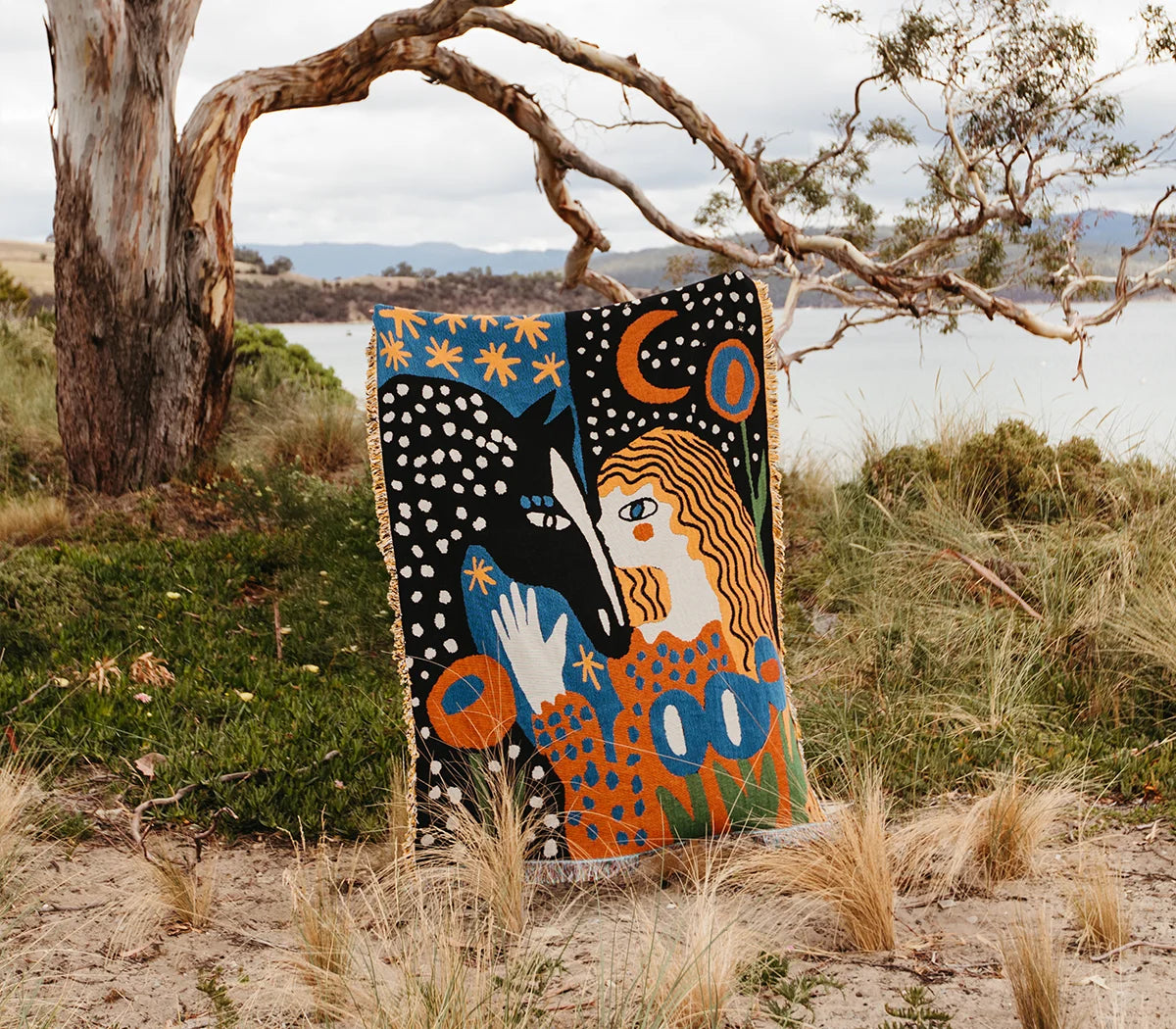 Colorful tapestry with abstract design in a natural setting with trees and water.