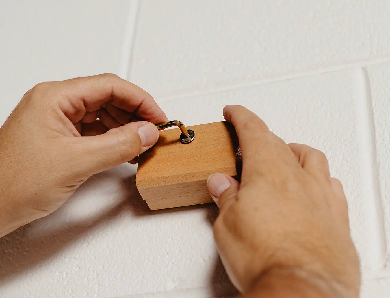 Person tightening the screw to fasten blanket hanger clip to wall using an Allen key. 