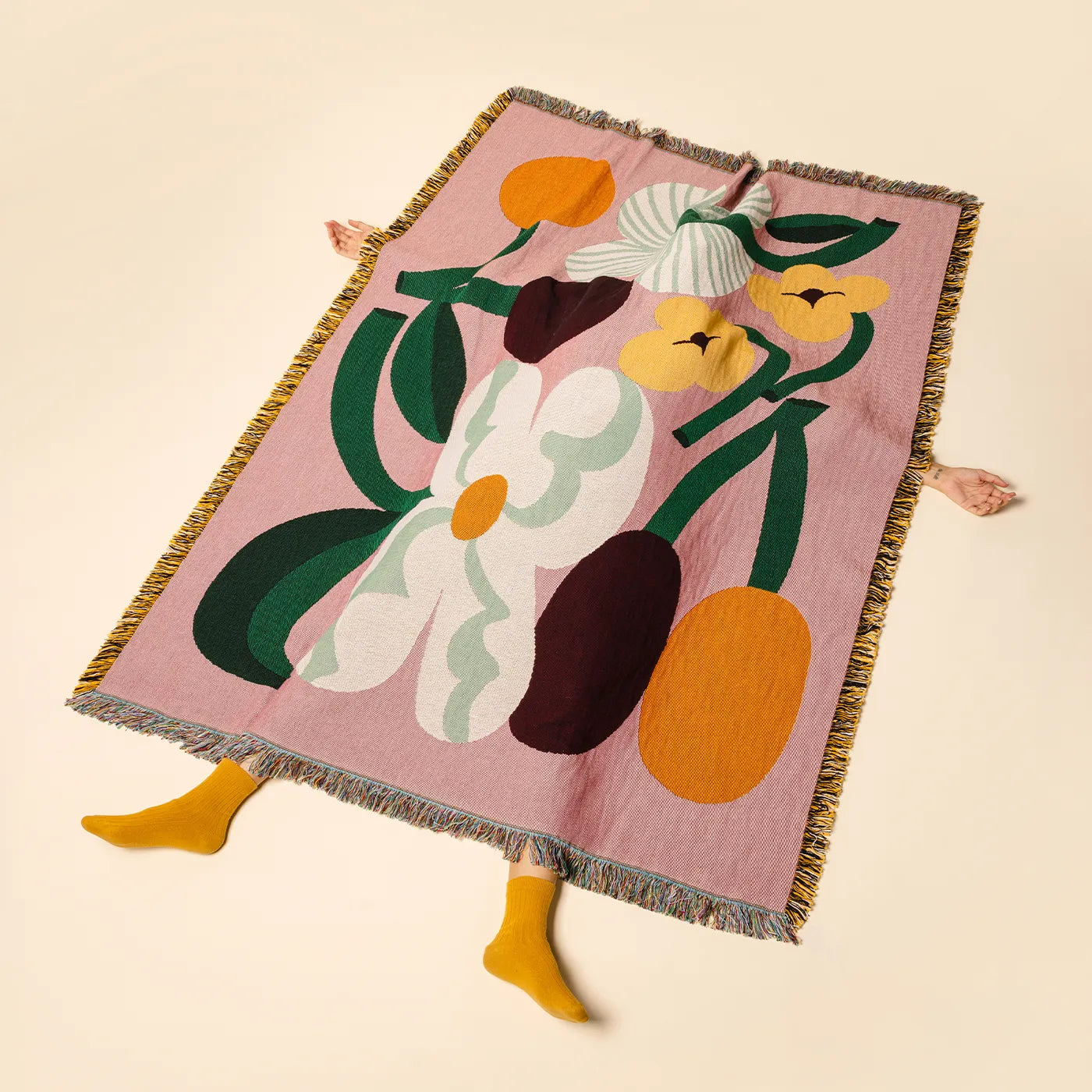 A pink woven throw blanket with fringe edges and a large floral pattern, styled with a person&