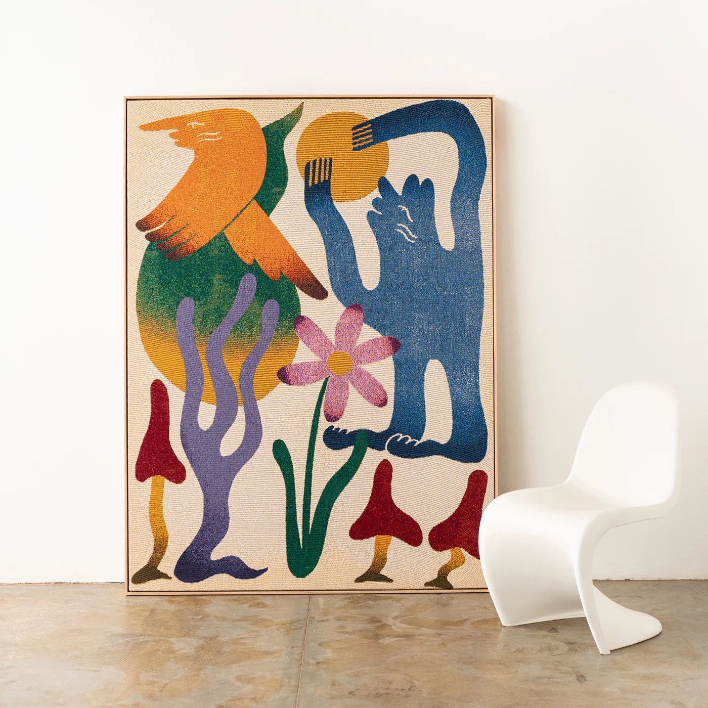 Colorful abstract artist-designed woven throw framed with an oak timber frame on a white wall with a modern curvy white chair.
