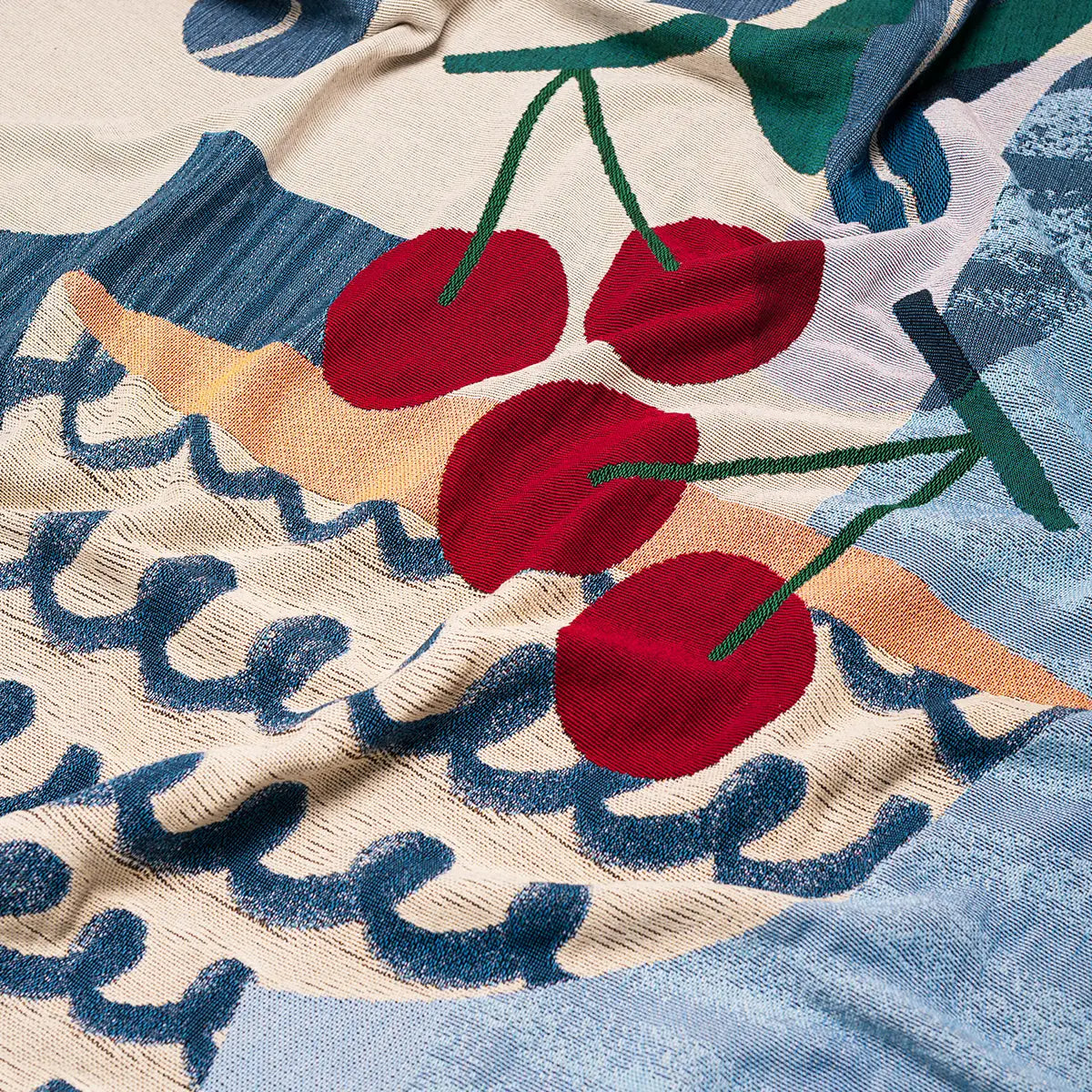 Close-up of a textured throw blanket with red cherries and abstract patterns.