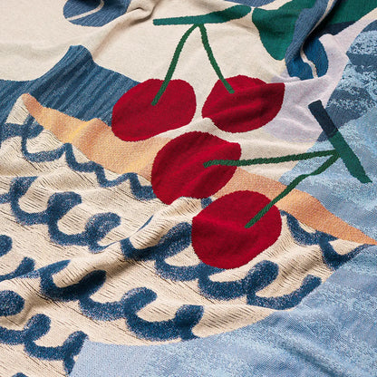 Close-up of a textured throw blanket with red cherries and abstract patterns.