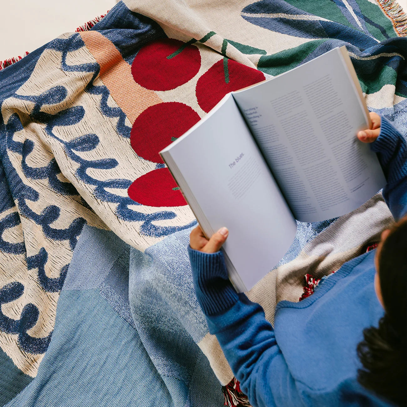 Person reading a book under a cozy blue and red throw blanket for couch