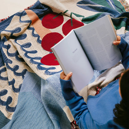 Person reading a book under a cozy blue and red throw blanket for couch