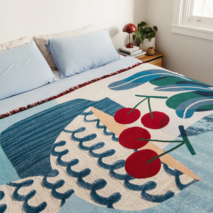 Decorative blue and red throw blanket with cherry design on a bed in a bedroom setting