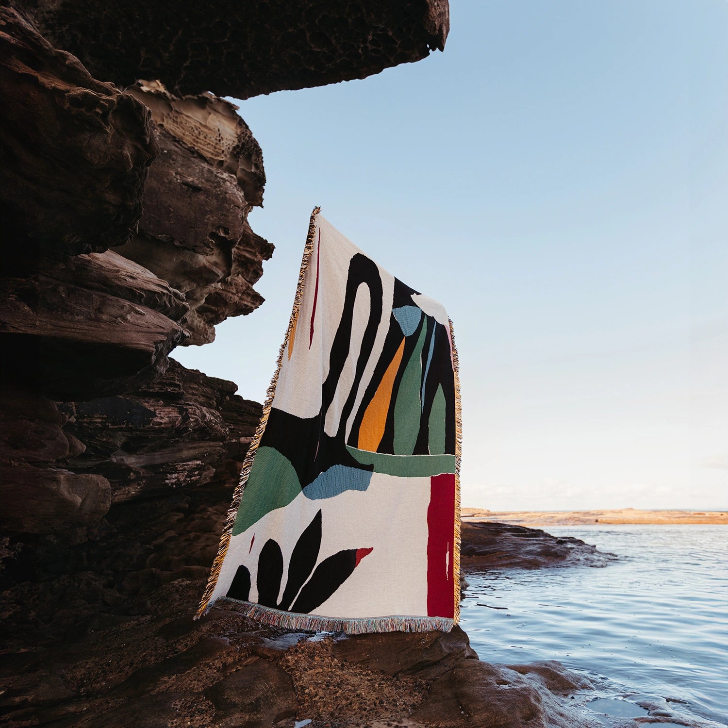 Colorful blanket with abstract patterns draped over a rock by the ocean.