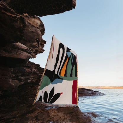 Colorful blanket with abstract patterns draped over a rock by the ocean.