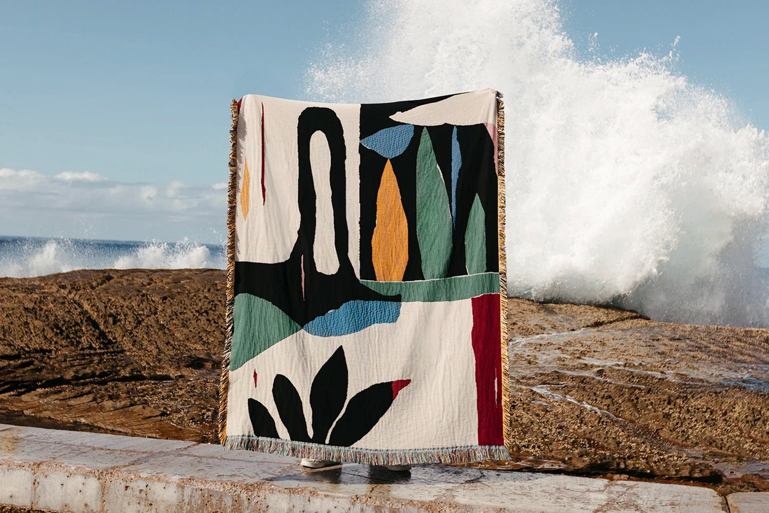Colorful abstract-patterned blanket draped over a chair by the ocean with waves crashing in the background