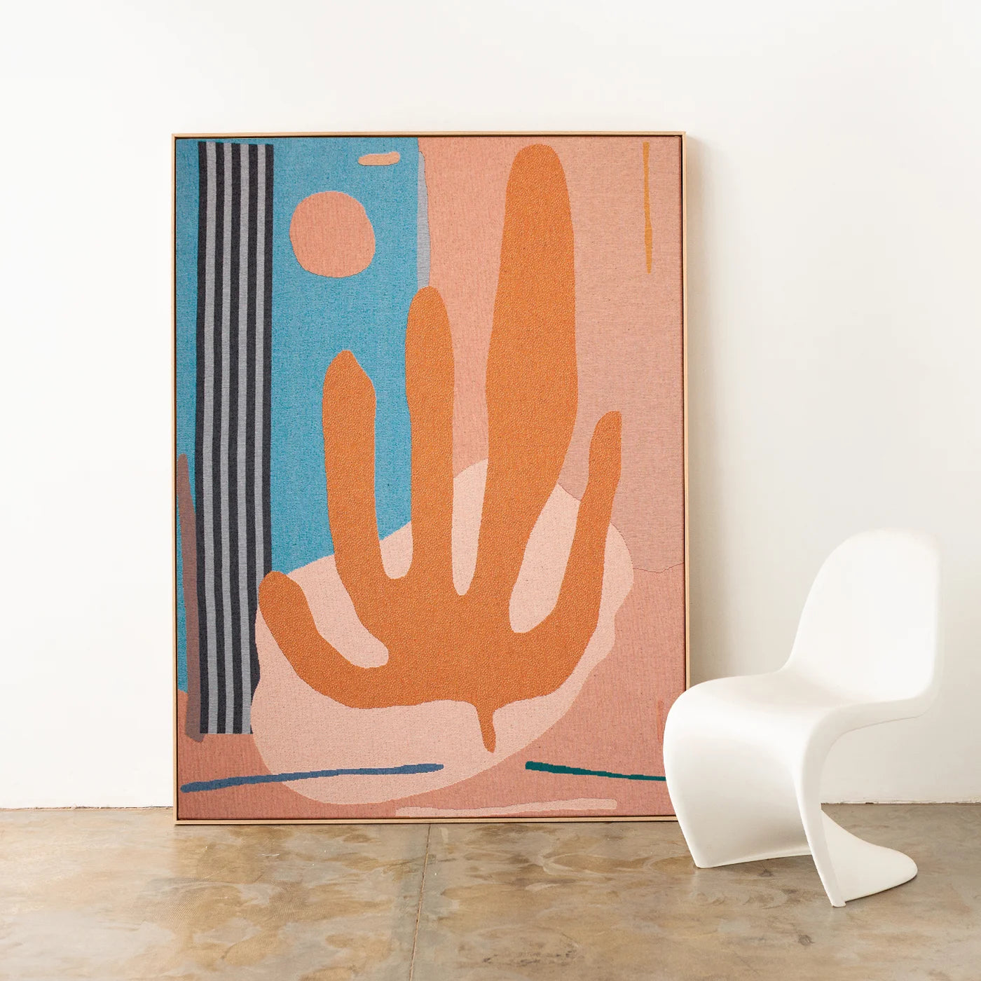 Desert inspired abstract artist-designed woven throw framed with an oak timber frame on a white wall with a modern curvy white chair.