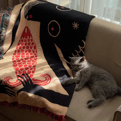 Gray cat lying on a couch with a decorative blanket featuring abstract designs.