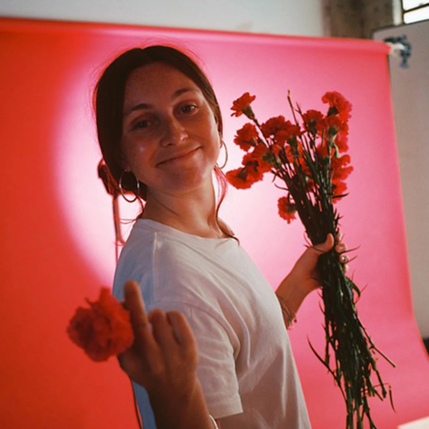 Portrait of English artist Imogen Sinclair holding orange flowers against a pink and red background