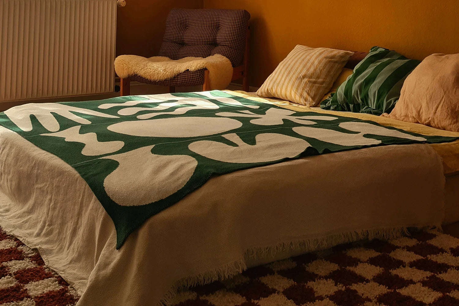 Bed with a green and white patterned blanket, pillows, and a chair in the corner.