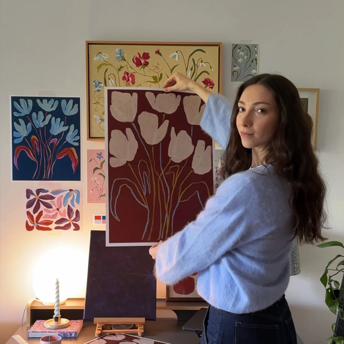 Portrait of English artist Louisa Taylor holding an art featuring painted flowers.