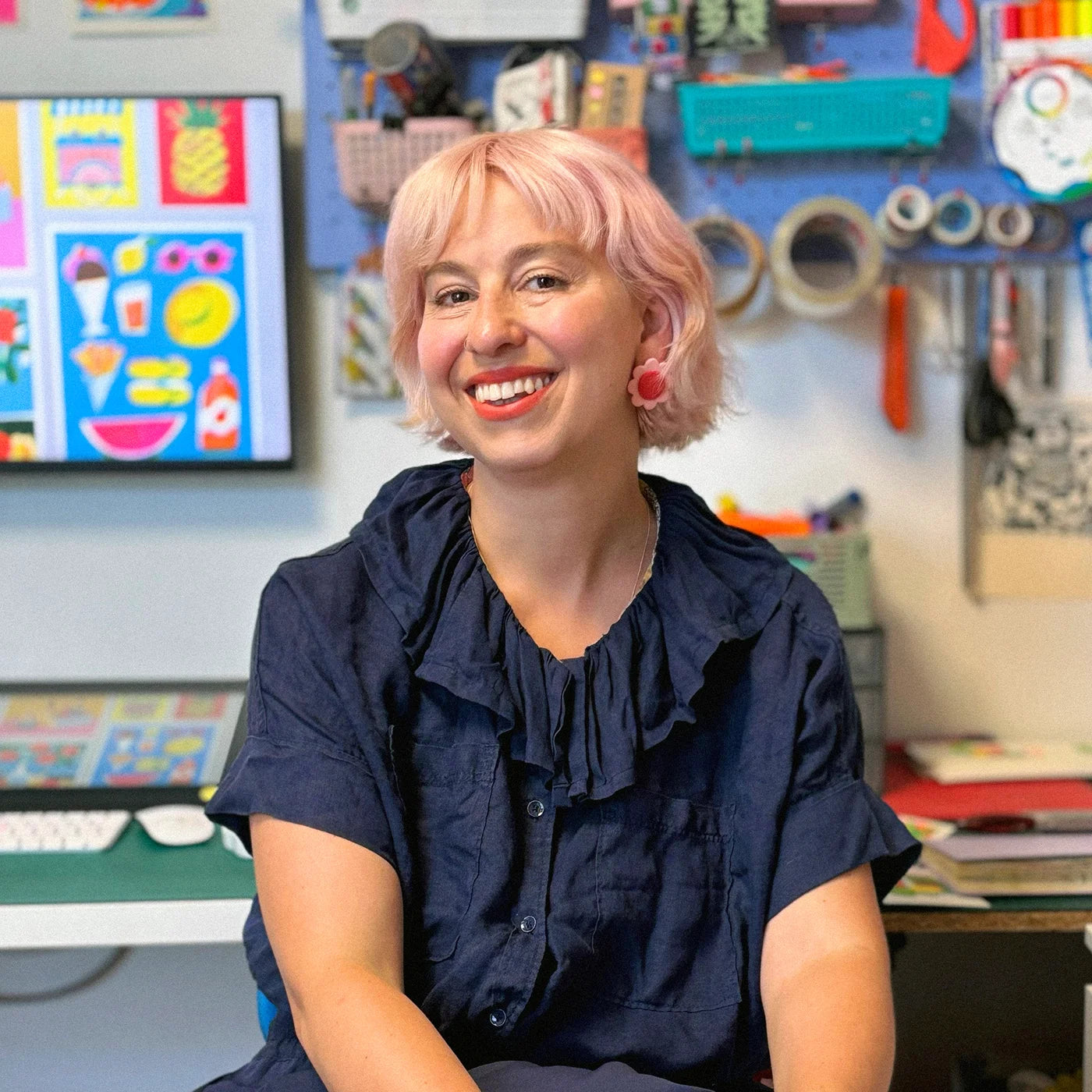 A portrait of a Italian artist Lucia Calfapietra smiling with short pink hair and wearing a dark navy ruffled blouse.