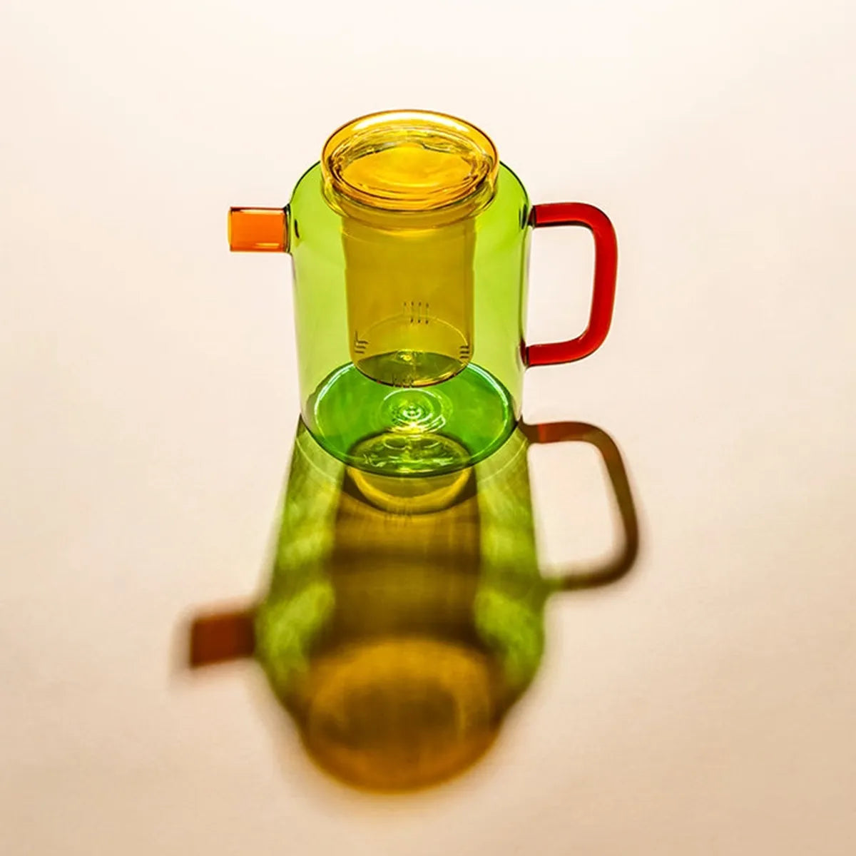 Green glass teapot with orange handle and spout on a white background