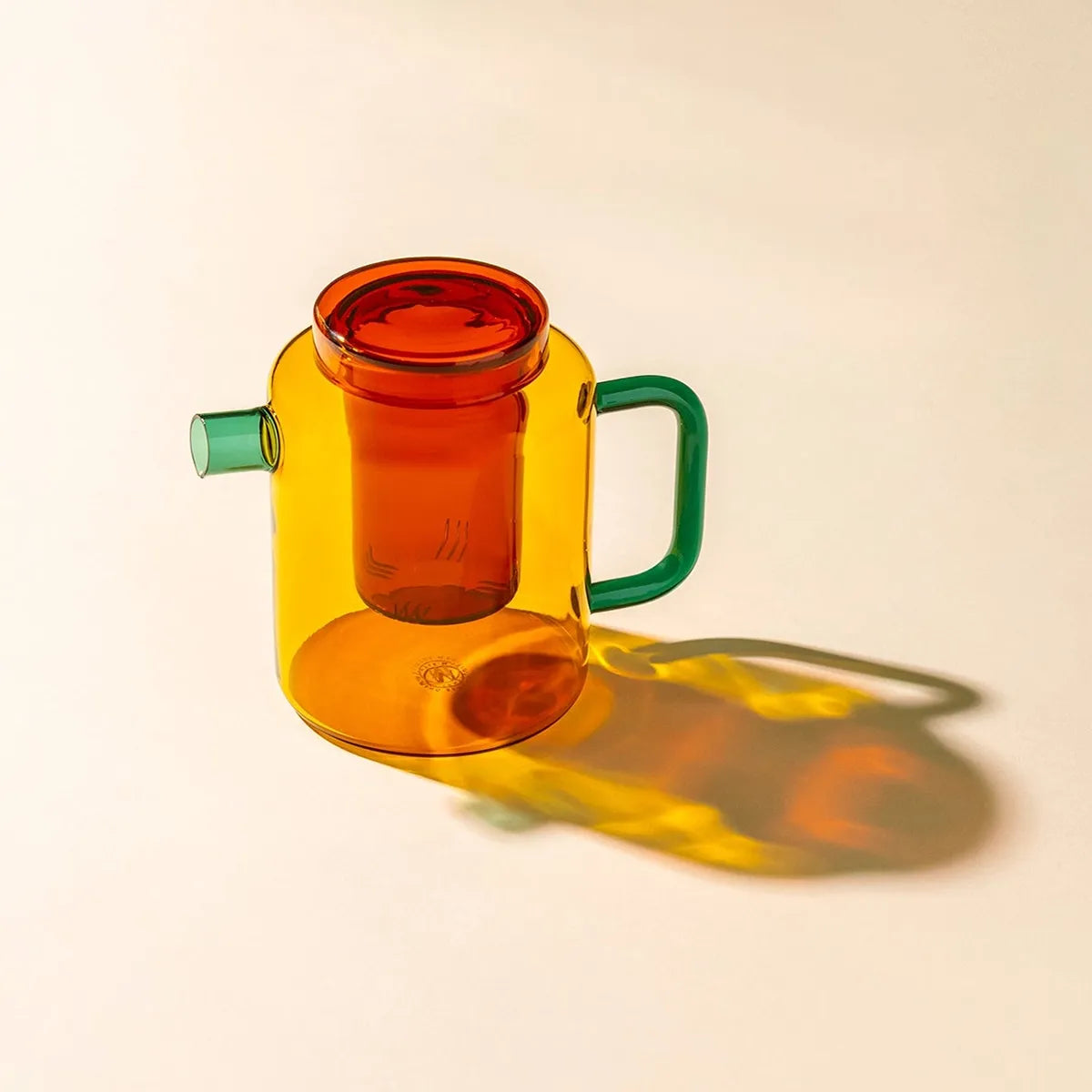 Orange glass teapot with teal handle and spout on a white background