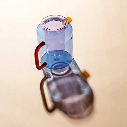 Blue glass teapot with orange handle and spout and pink diffuser and lid on a beige background