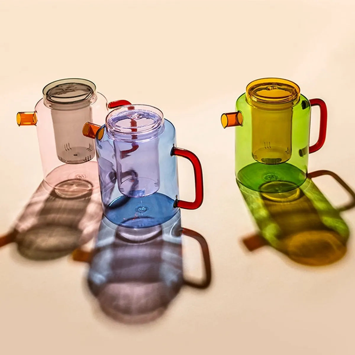 Three colorful glass teapots on a beige background