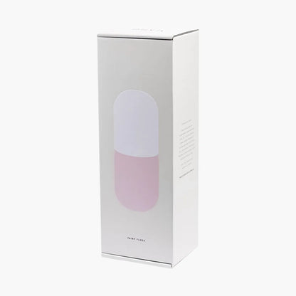 White box with a pink glass carafe and white cup set inside on a white background