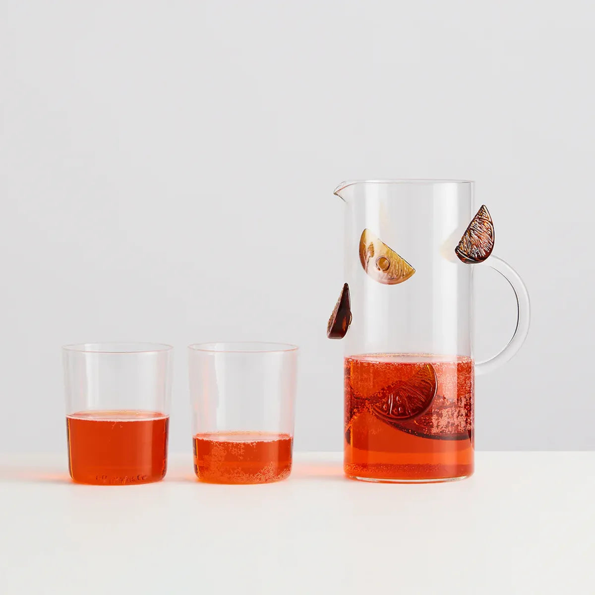 Glass pitcher and two glasses filled with a red liquid on a white background