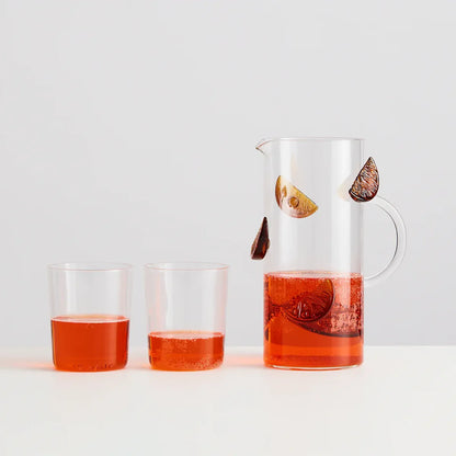 Glass pitcher and two glasses filled with a red liquid on a white background
