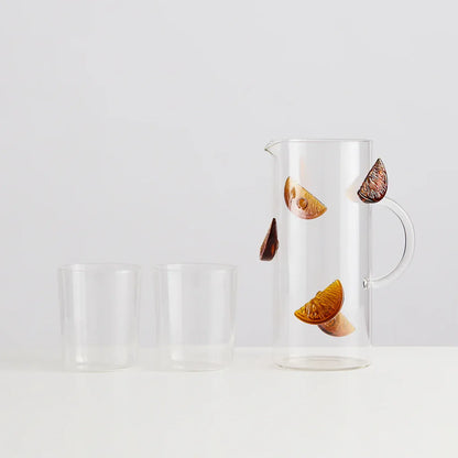 Clear glass pitcher and two glasses with orange slice design on a gray background