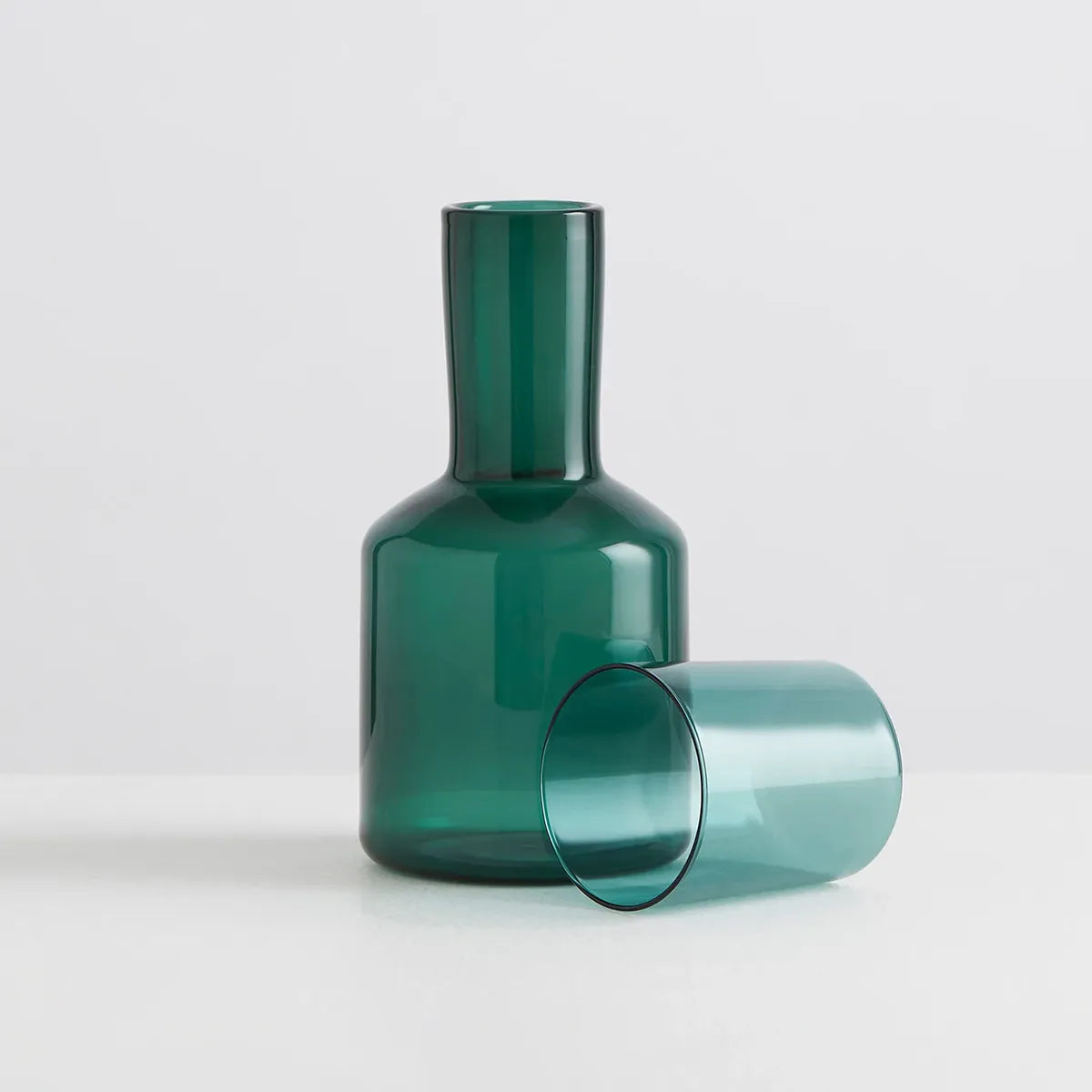 Green glass carafe and tumbler on a light gray background