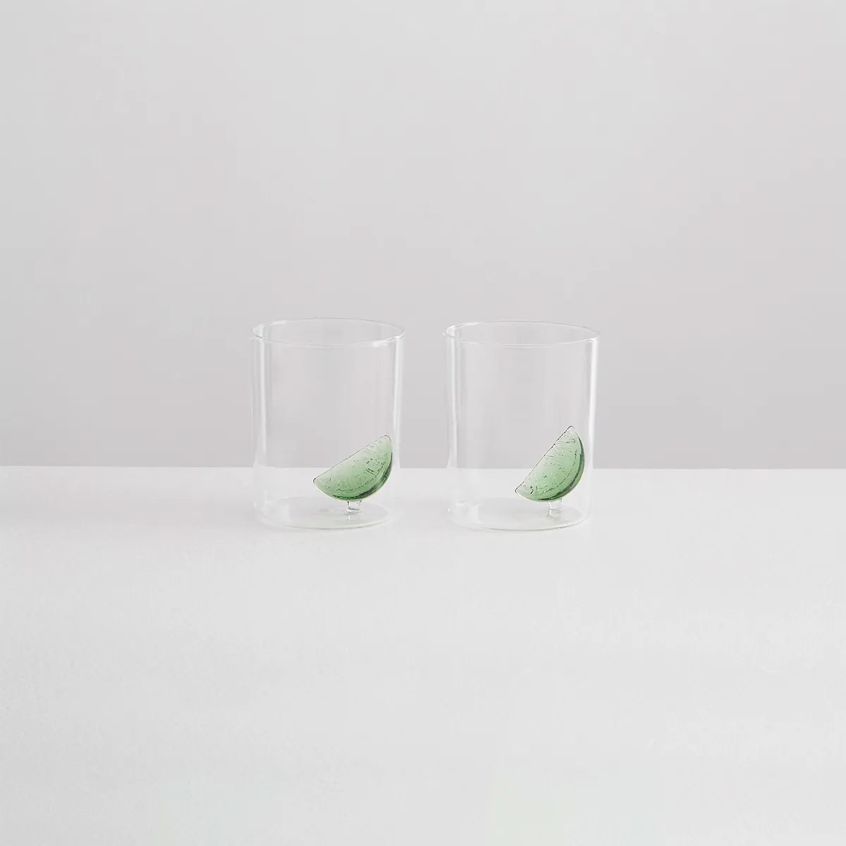 Two clear glasses with green leaves on a white background