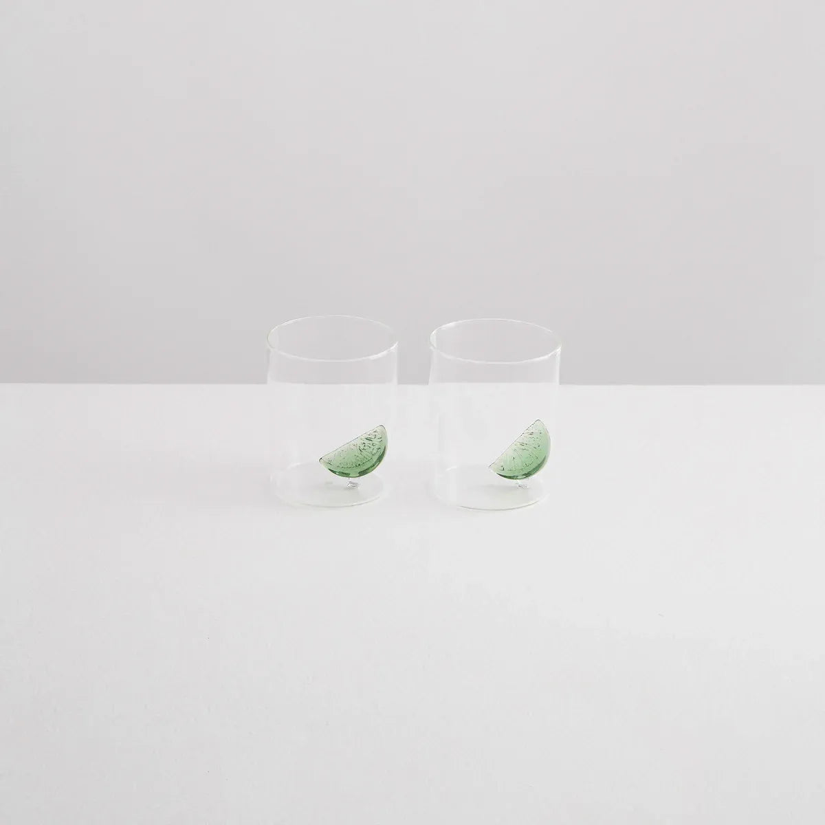 Two clear glass tumblers with green leaves on a light gray background