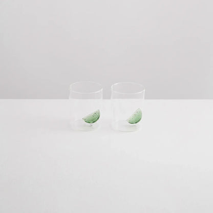 Two clear glass tumblers with green leaves on a light gray background