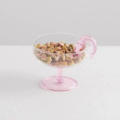 Clear glass prawn cocktail coupe with pink stem filled with colorful nuts on a white background