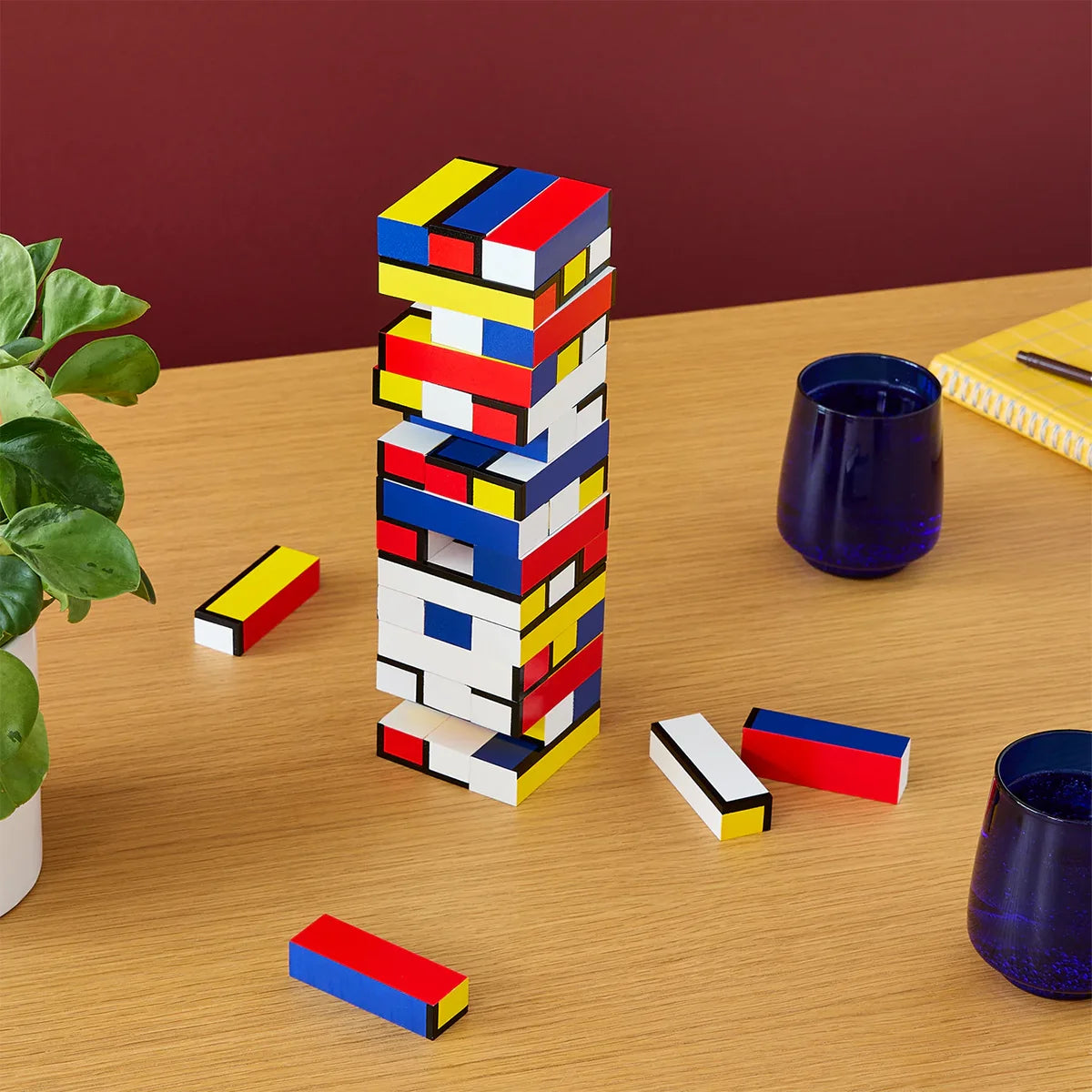 Colorful geometric tower building blocks on a wooden table with a plant and cups in the background.
