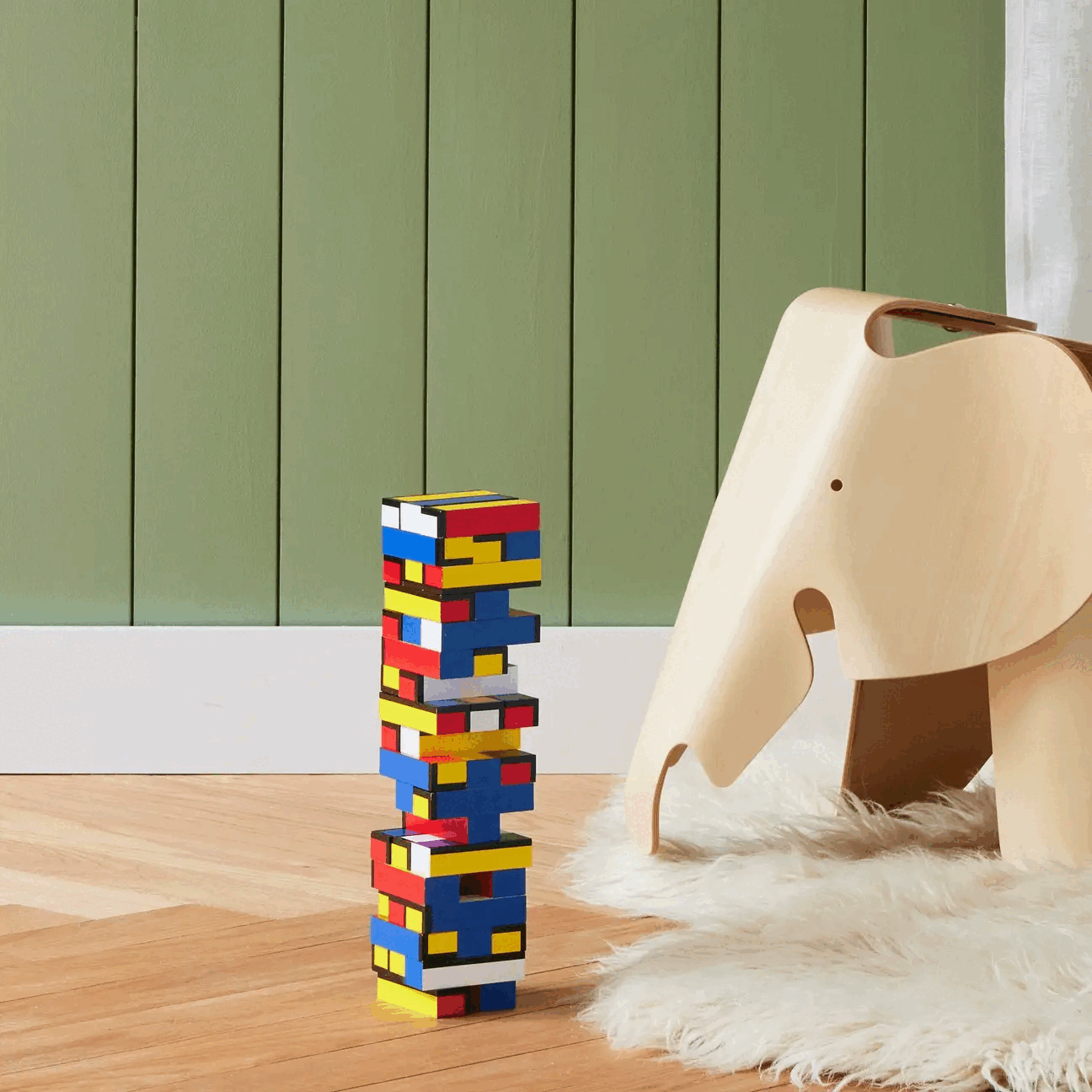 Looping video of a colorful geometric block tower and wooden elephant on a wooden floor in front of a green background