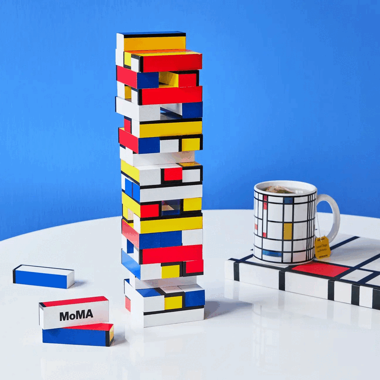 Looping video of a colorful geometric block tower and a matching mug and notebook on a white table in front of a blue background