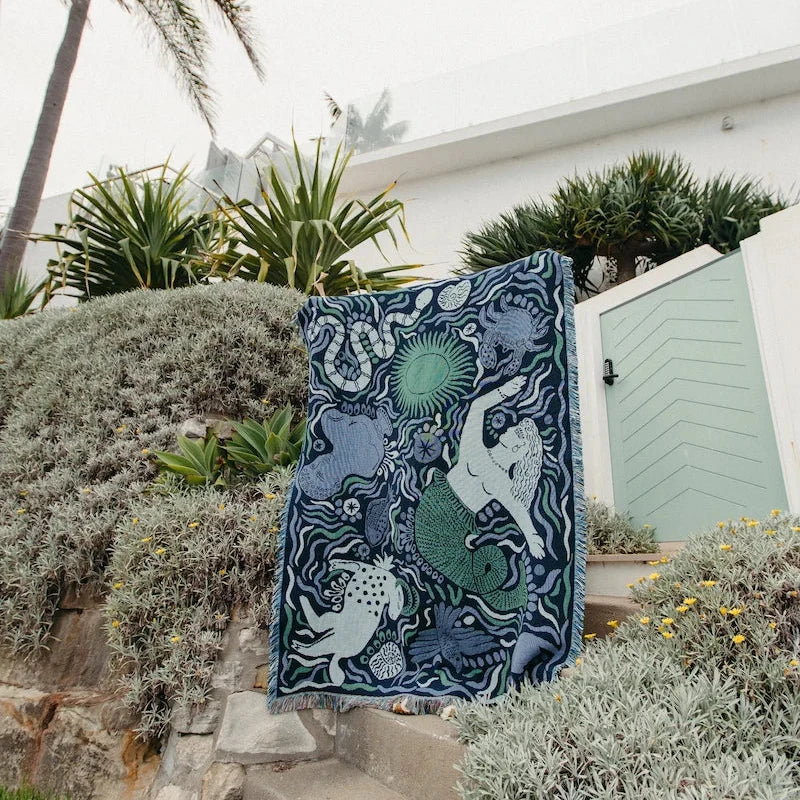 Decorative blue throw blanket with mermaid design on a stone staircase outdoors