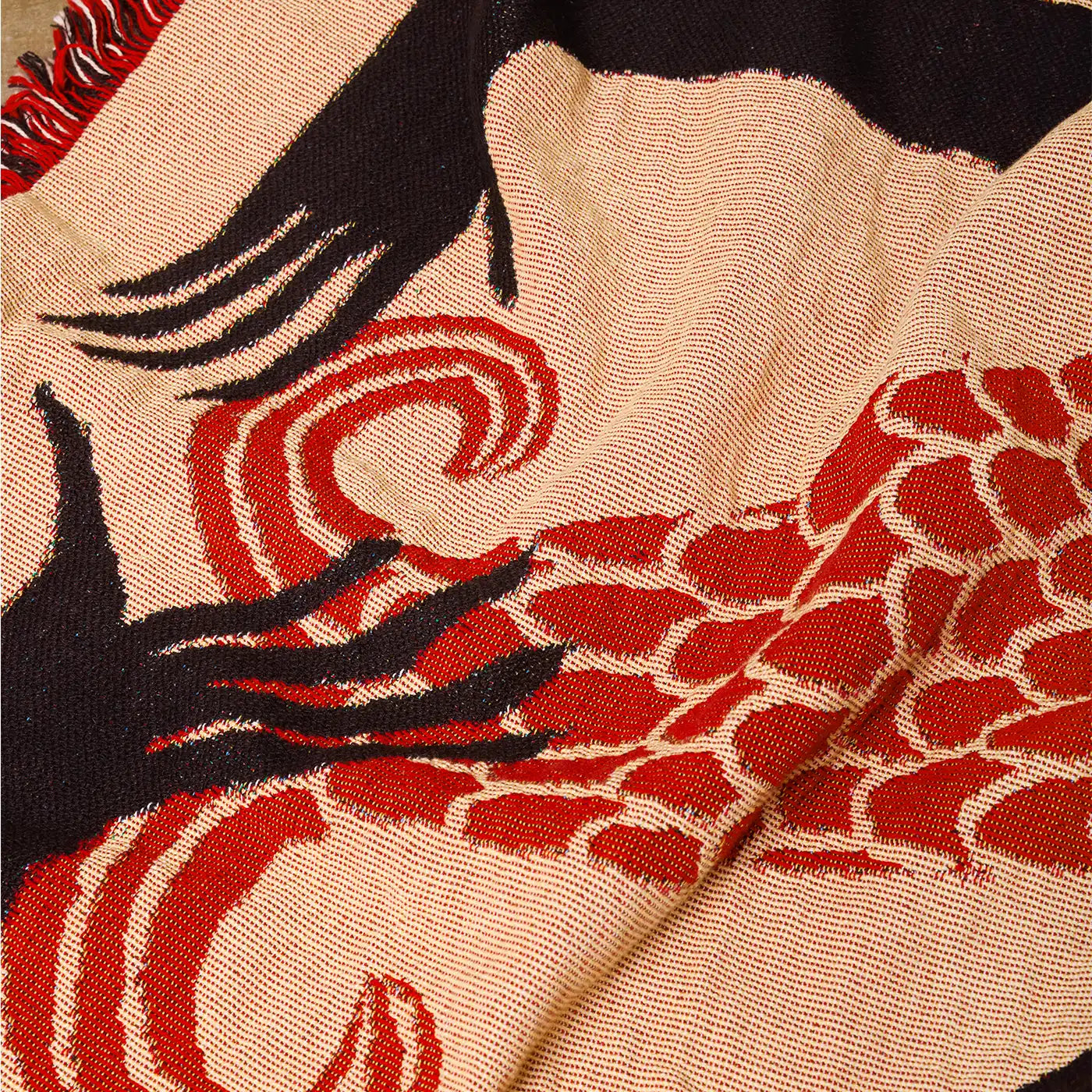 Close-up of a knit blanket fabric with red, black, and beige abstract patterns.