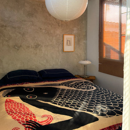 Bed with a decorative throw featuring a mermaid and fish folklore design in a bedroom setting.