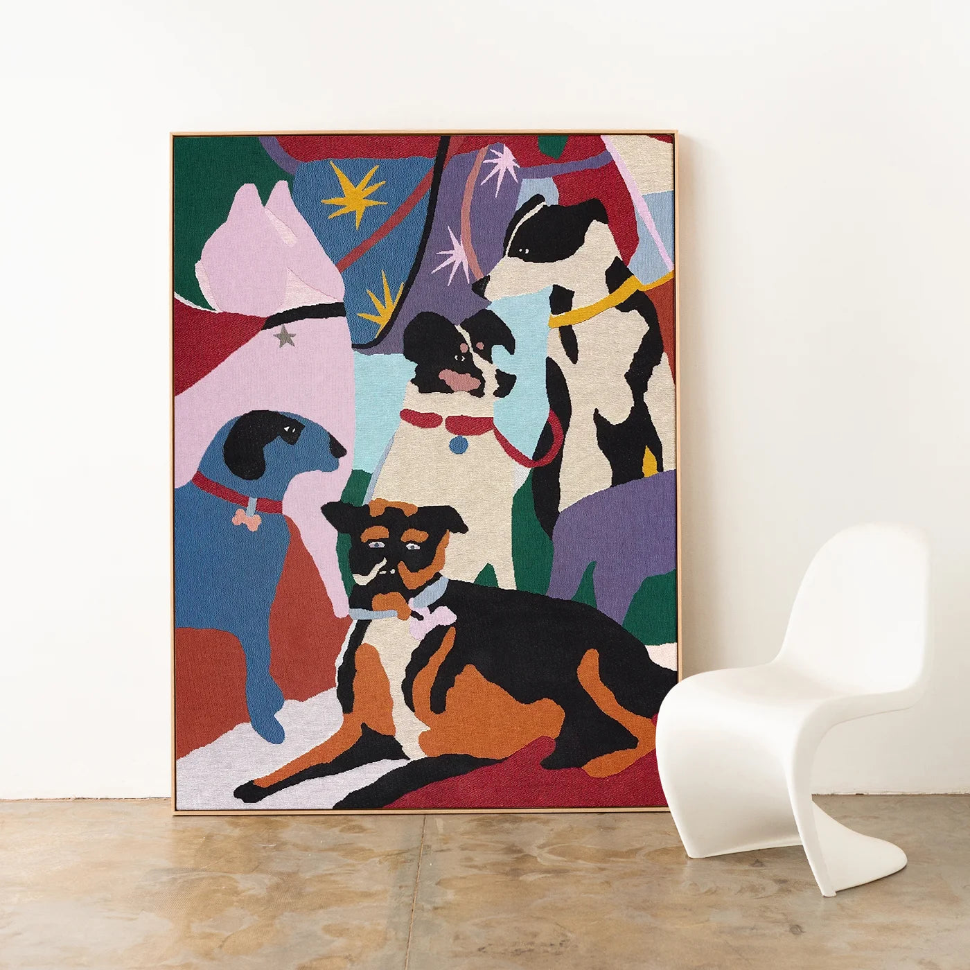Colourful artist-designed woven throw featuring dog illustrations, framed with an oak timber frame on a white wall with a modern curvy white chair.